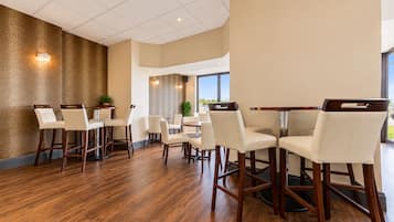 Un amplio comedor con piso de madera, sillas blancas tapizadas y un gran ventanal con vistas al exterior.