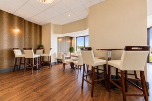 Un amplio comedor con piso de madera, sillas blancas tapizadas y un gran ventanal con vistas al exterior.