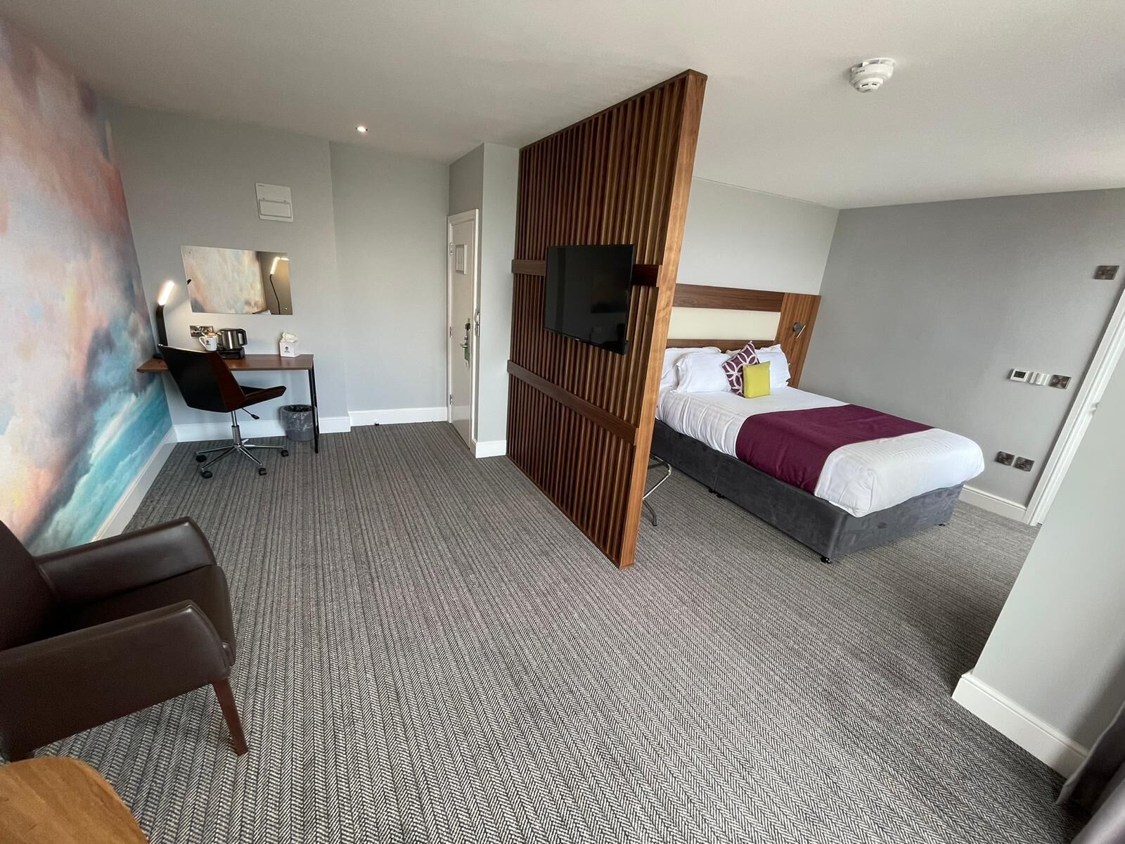 Quarto de hotel com cama, escrivaninha, cadeira e uma grande pintura na parede.