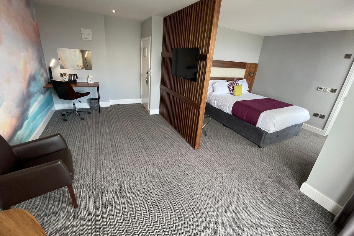 A hotel room with a bed, desk, chair, and a large painting on the wall.
