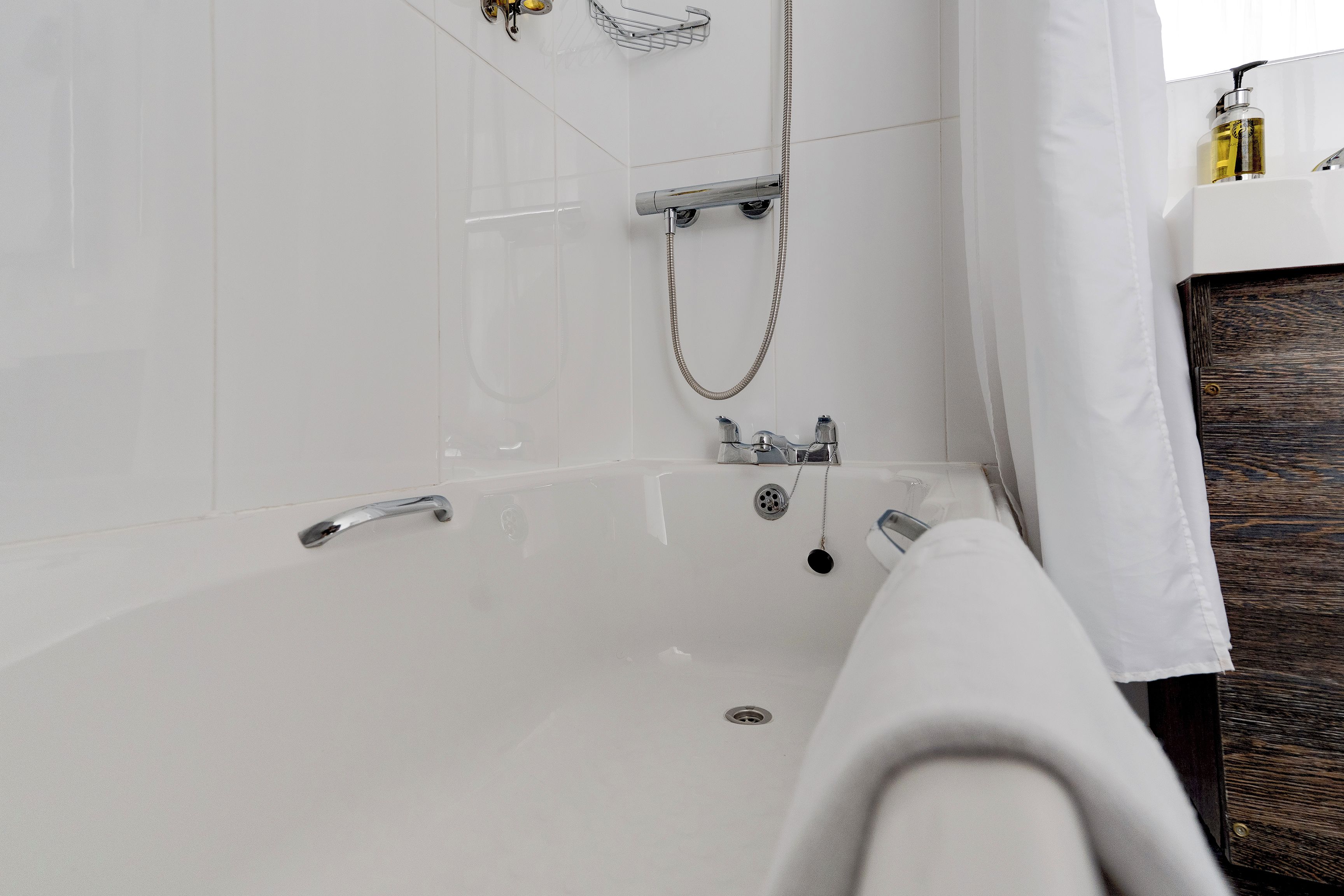 Een moderne badkamer met een witte badkuip, een douchekop en een handdoekrek.