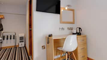 A hotel room with a wooden desk, a white chair, a flat-screen TV mounted on the wall, a wooden-framed mirror, and a coffee maker on the desk.