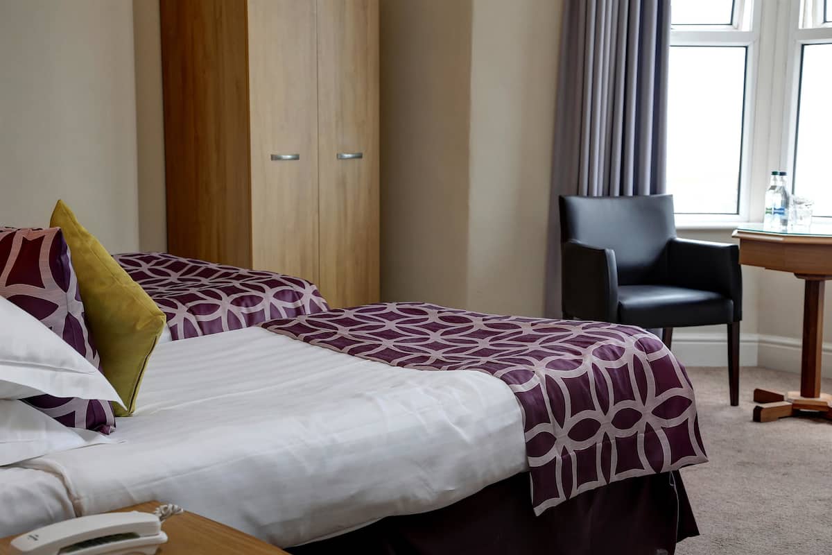 Habitación de hotel con dos camas, un armario de madera, una silla negra y una mesita con botellas de agua.