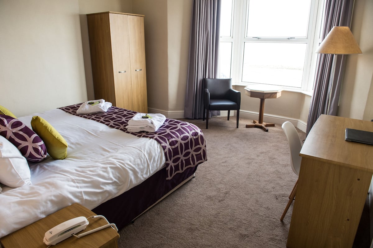 Una habitación de hotel con una cama, un armario de madera, un escritorio y una silla.