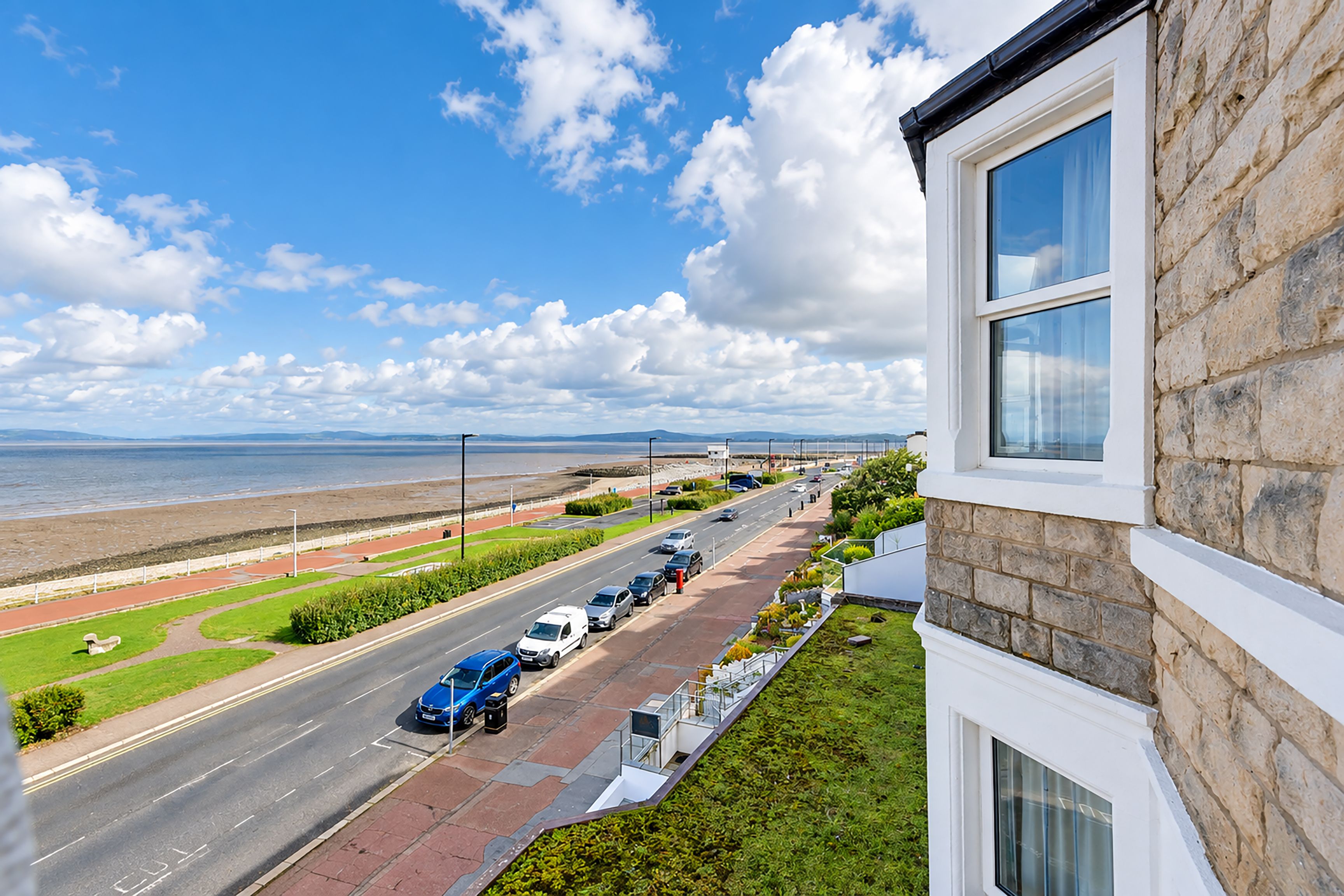 A coastal road with parked cars, a clear sky, and a view of the sea.