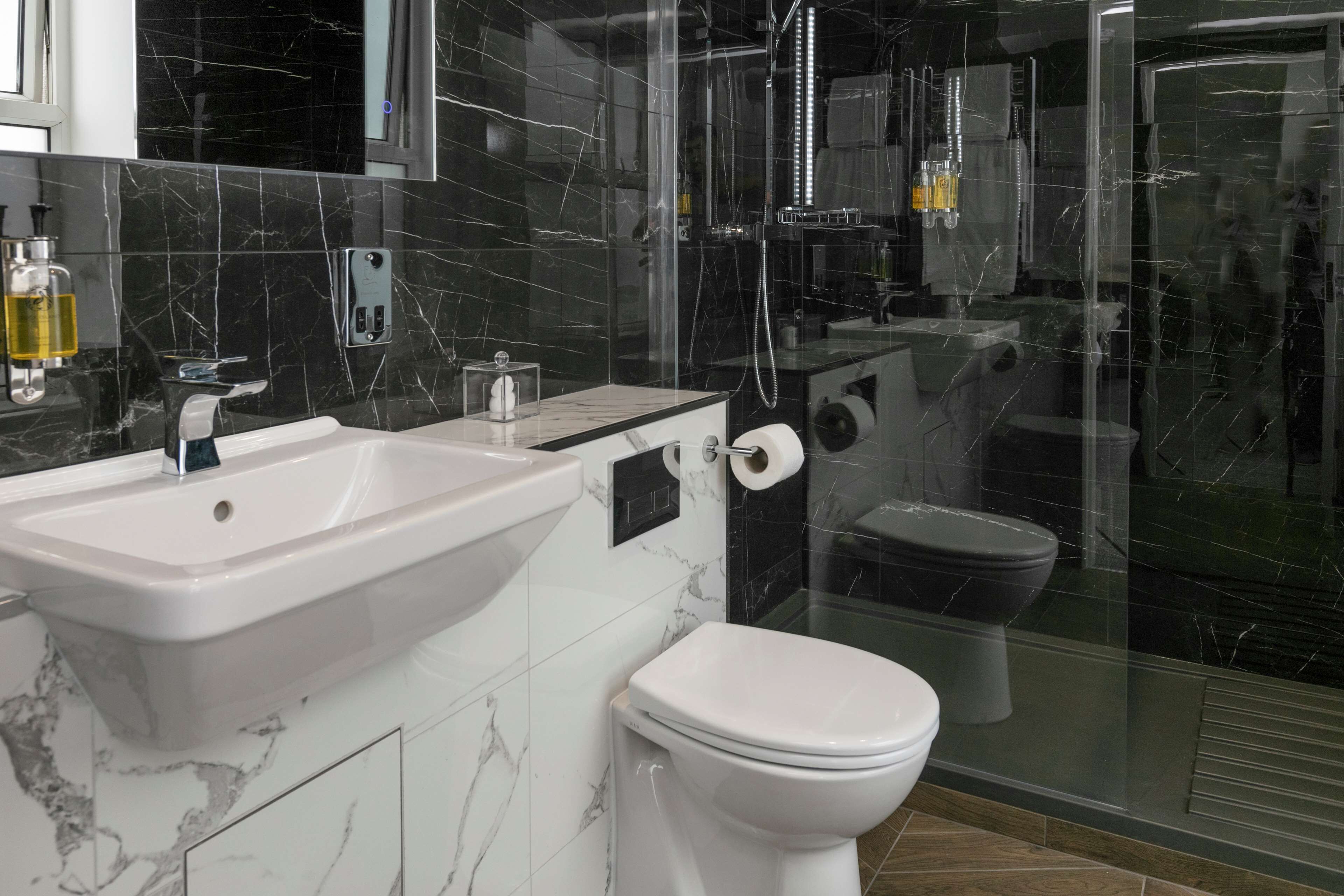 A modern bathroom with a white sink, toilet, and glass shower enclosure.