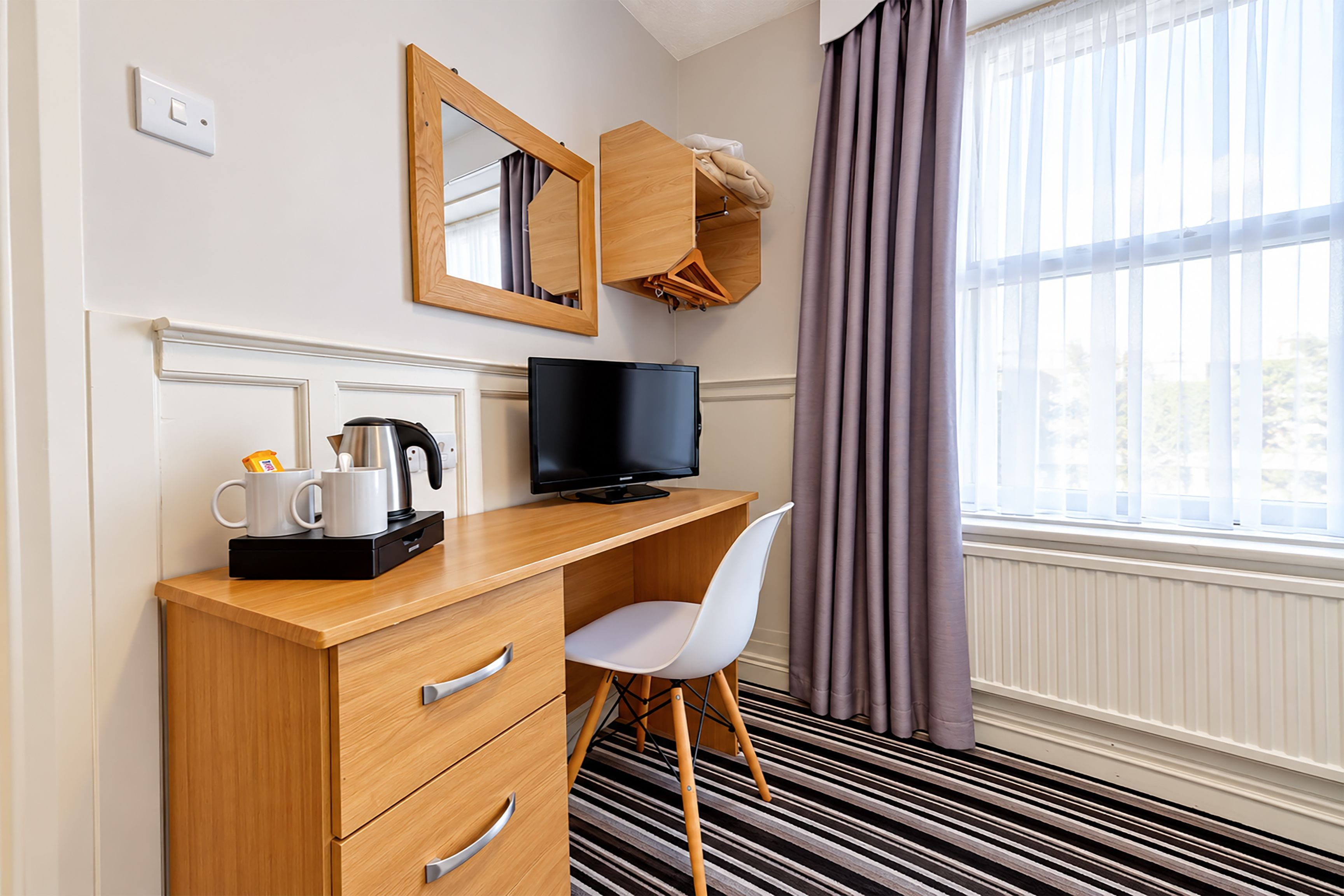 A hotel room with a wooden desk, a television, a chair, a coffee maker, and a mirror.