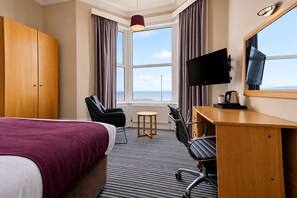 Una habitación de hotel con cama, escritorio, silla, televisión y vista al mar.