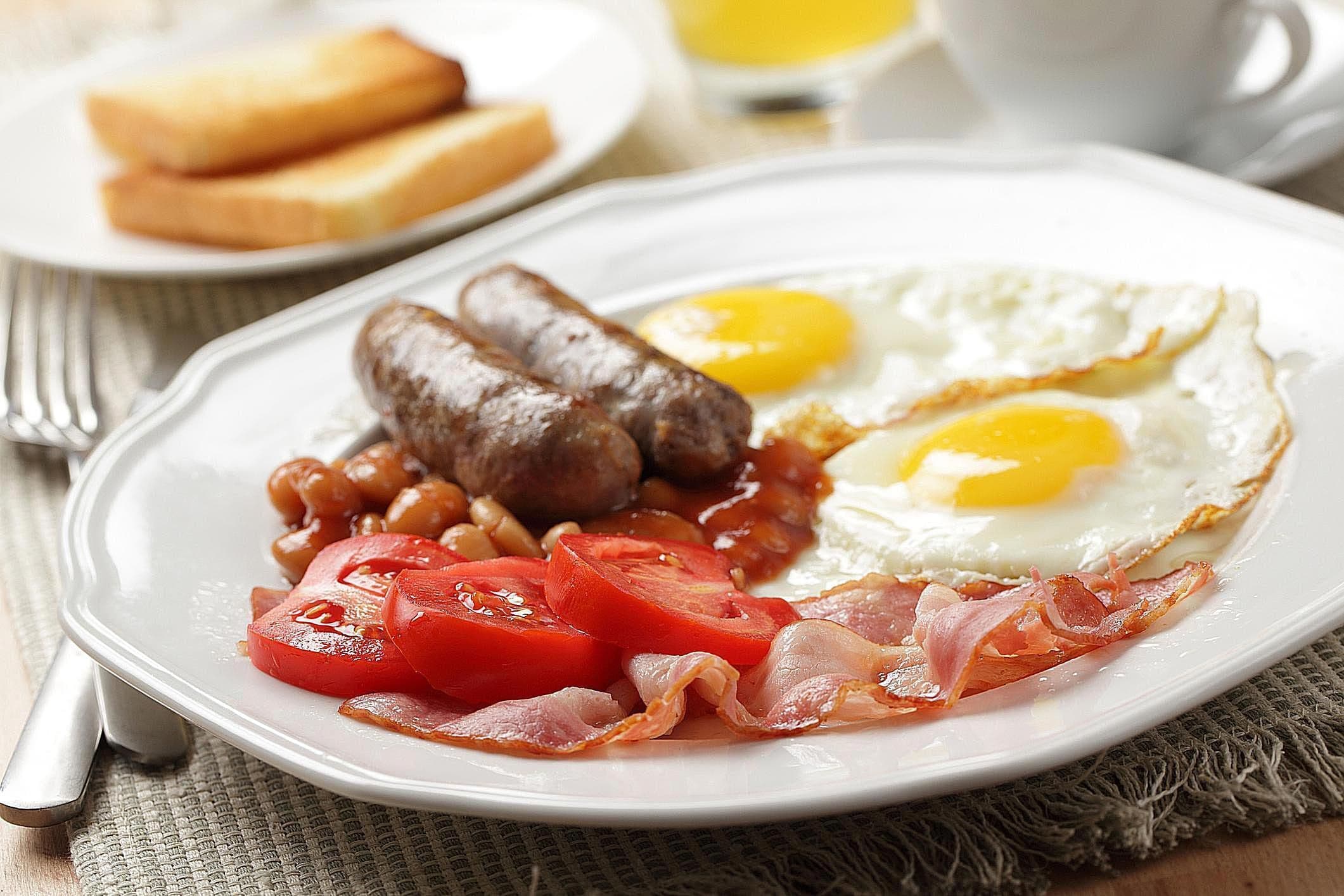 A plate with eggs, sausages, bacon, tomatoes, and beans.