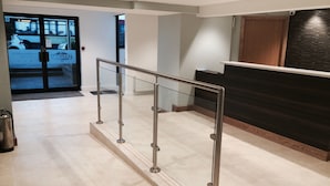 A modern reception area with a glass railing, a wooden reception desk, and a view of the street through glass doors. - Lothersdale Hotel Morecambe by Belvilla (Morecambe)