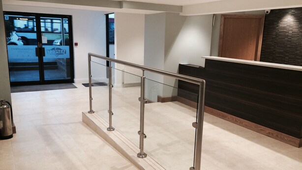 A modern reception area with a glass railing, a wooden reception desk, and a view of the street through glass doors. - Lothersdale Hotel Morecambe by Belvilla (Morecambe)