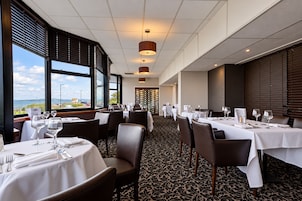 A restaurant with tables set for dining, large windows offering a view, and a patterned carpet.