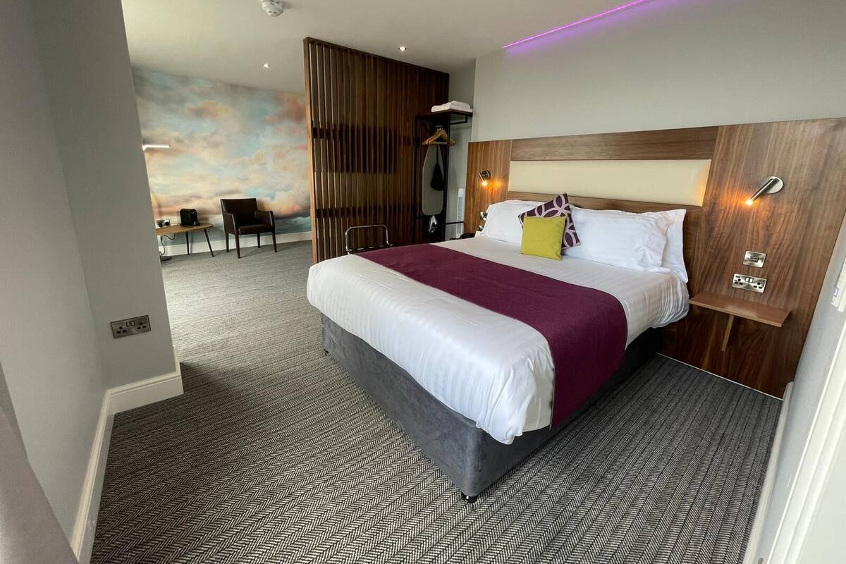 Una habitación de hotel moderna con una cama grande, un cabecero de madera, un escritorio y una silla.