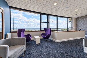 Un área de espera moderna con grandes ventanales, vista al mar y un mostrador de recepción.