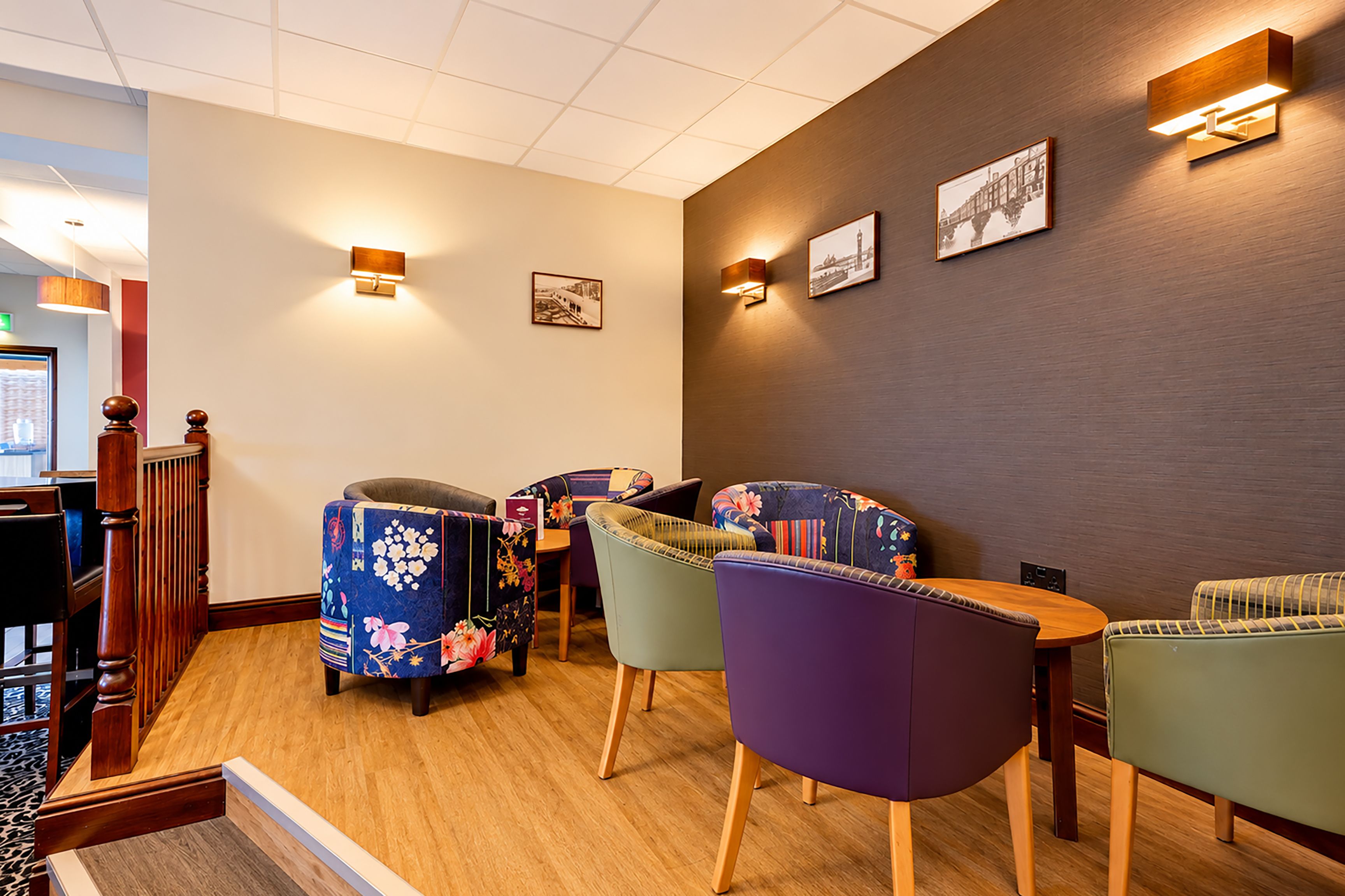Habitación de hotel con escalera de madera, zona de comedor con sillas de colores y obras de arte colgadas en la pared.
