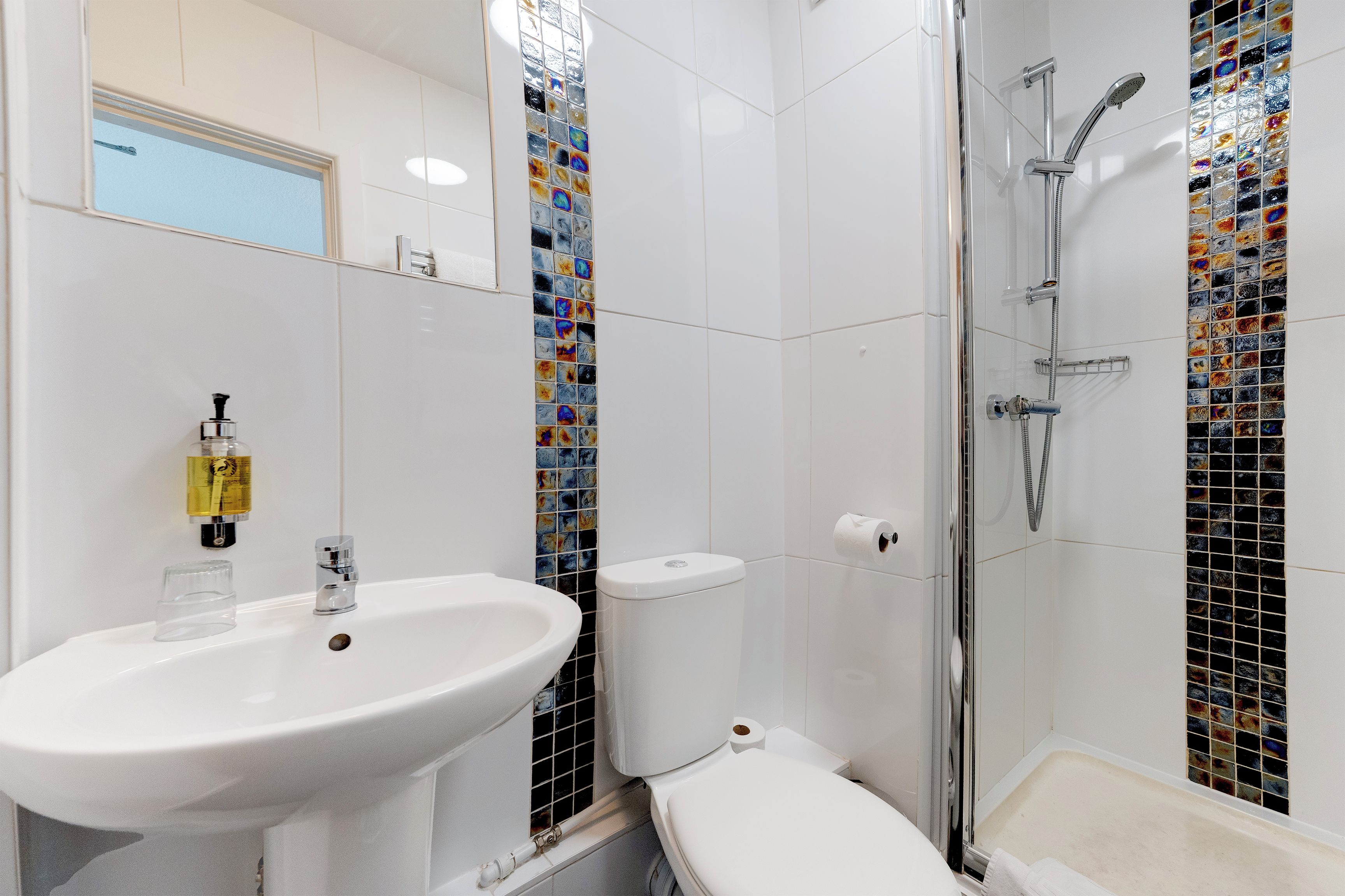 Un baño con lavamanos, inodoro y ducha blancos.