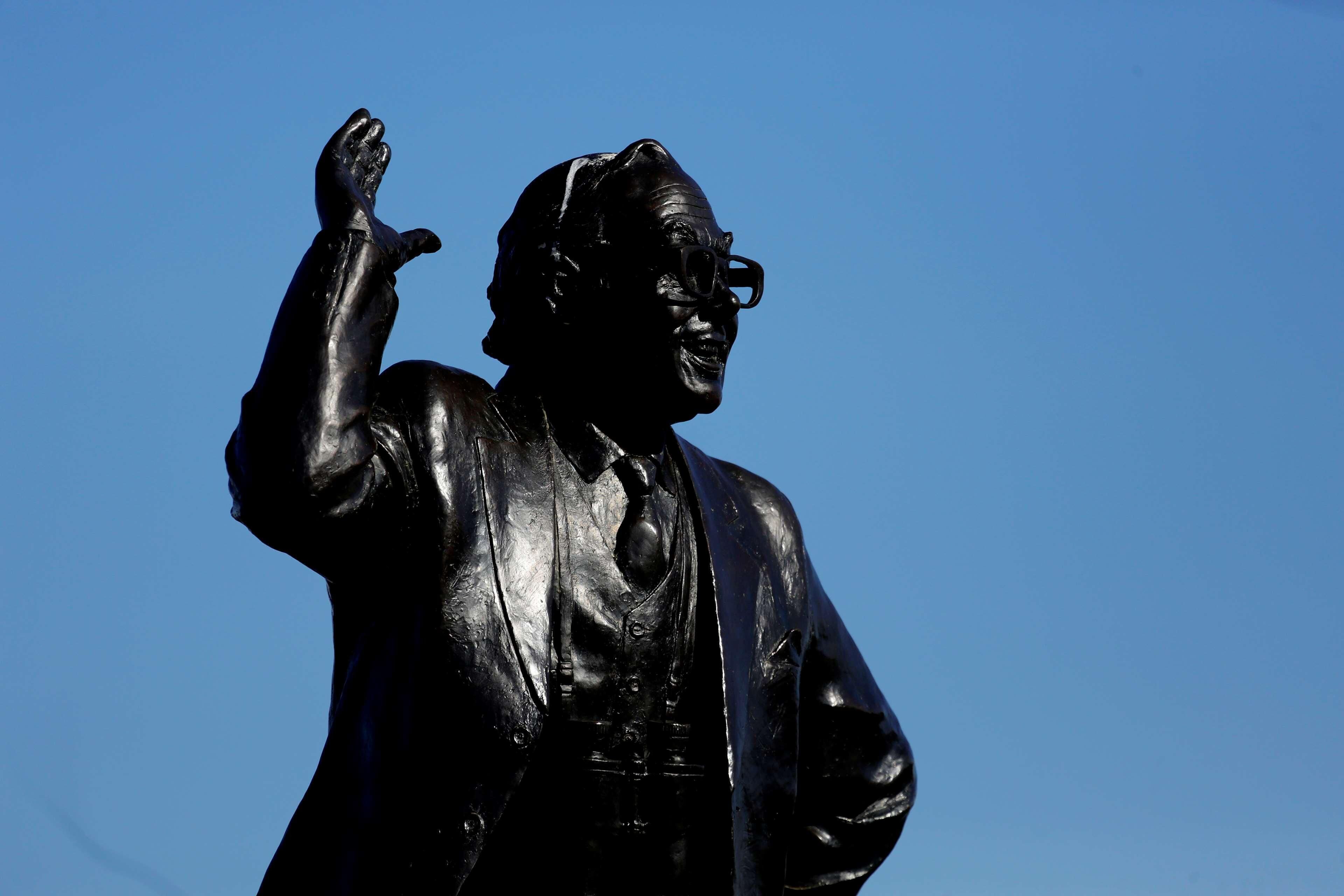 A statue of a man with a raised hand, set against a clear blue sky.