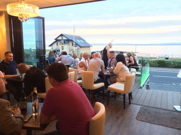 A restaurant with outdoor seating overlooking a body of water, featuring a chandelier and a view of a house in the background. - Lothersdale Hotel Morecambe by Belvilla (Morecambe)
