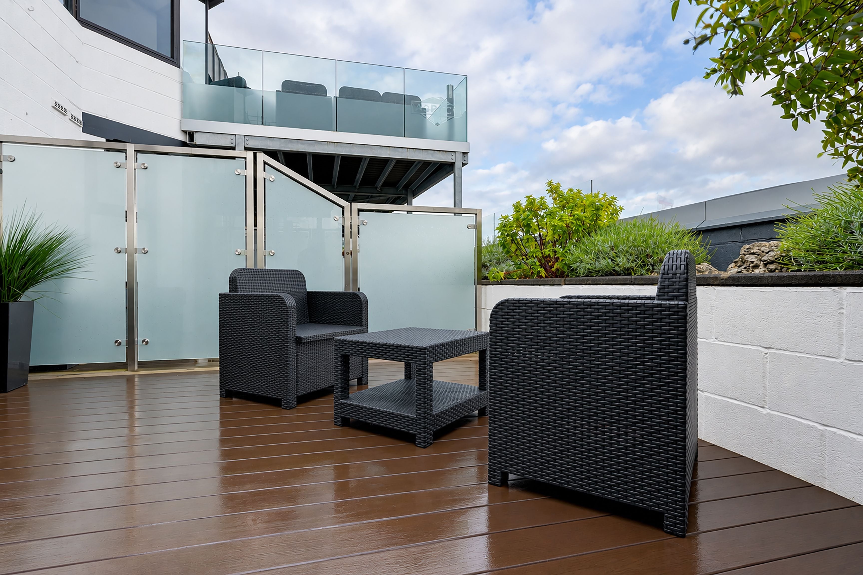A patio area with wicker furniture, a glass balustrade, and a white wall.
