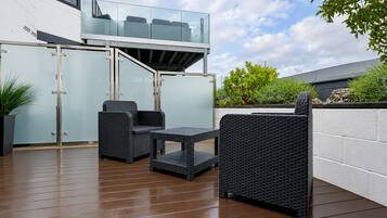 A patio area with wicker furniture, a glass balustrade, and a white wall.