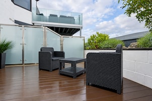 A patio area with wicker furniture, a glass balustrade, and a white wall.