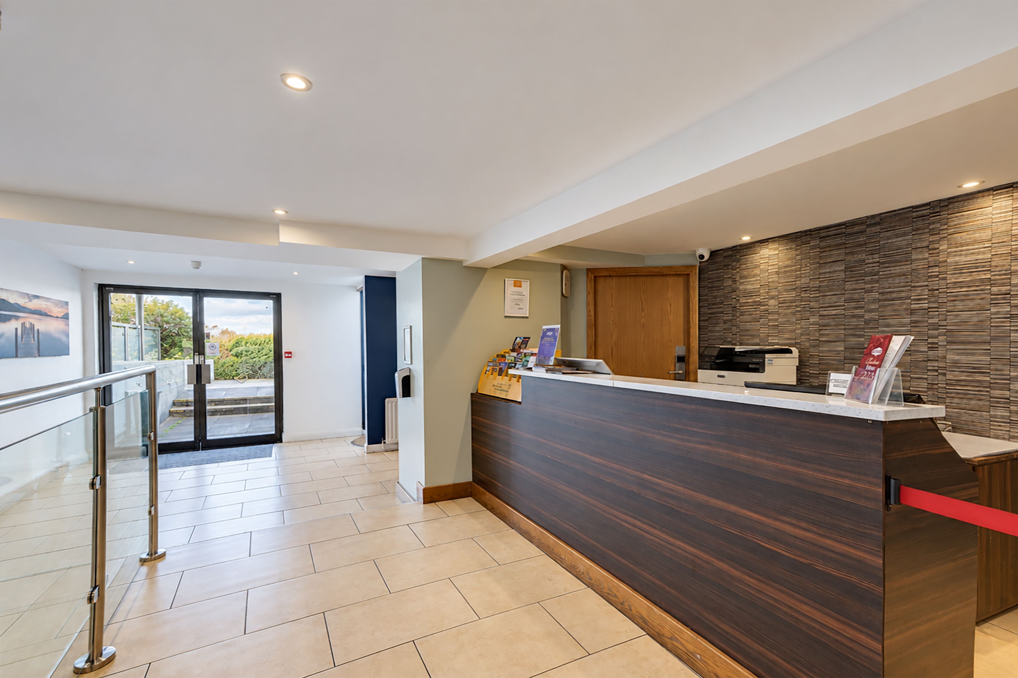 Una moderna zona de recepción con un mostrador de madera, puerta de cristal de entrada y vistas al exterior.