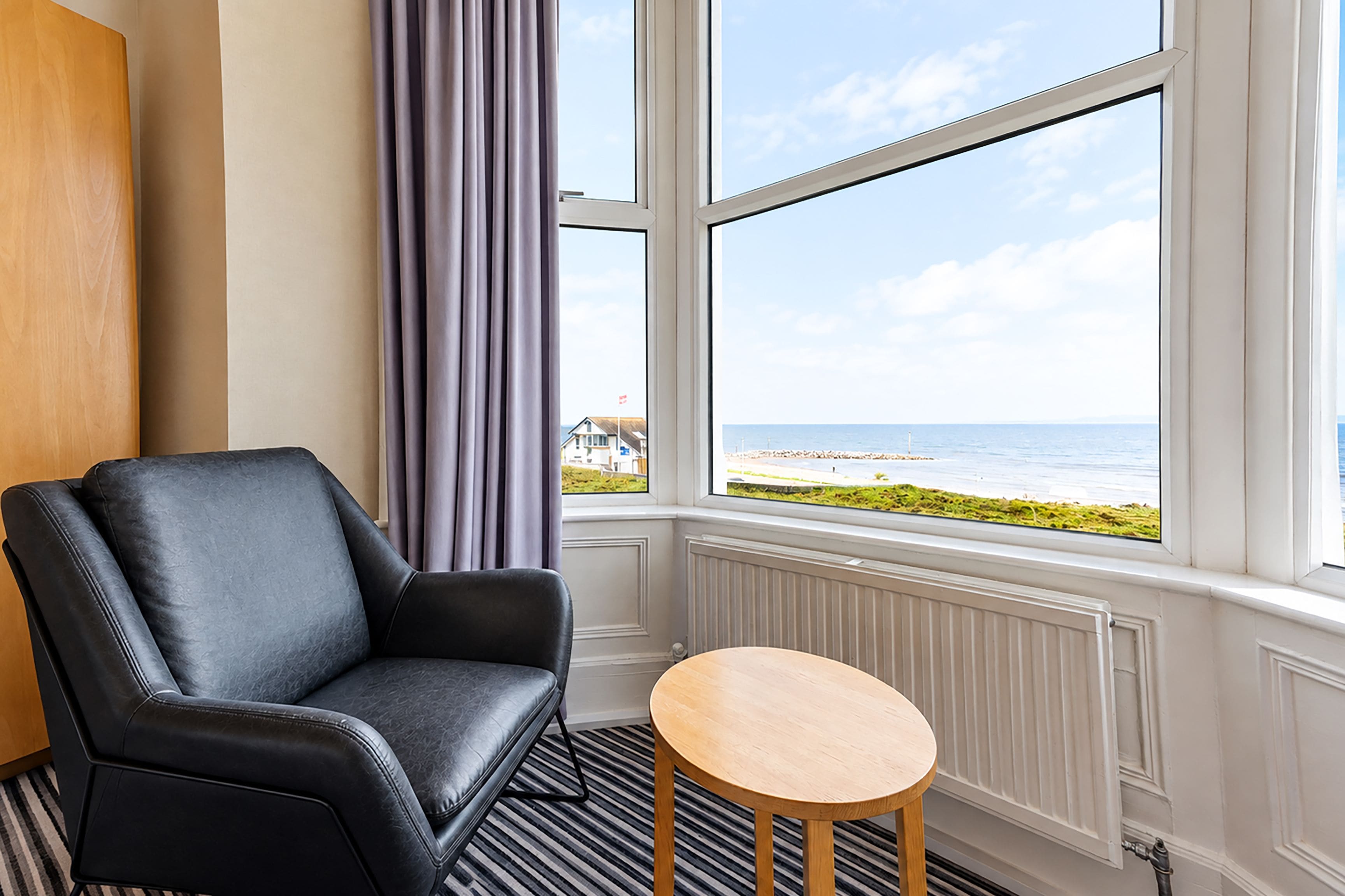 Una habitación con un sillón de cuero negro, una mesita de madera y vistas al mar a través de un ventanal grande.
