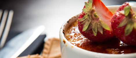 Een dessert met een aardbei erop, een koekje ernaast, en een mes en lepel op een donkere ondergrond.
