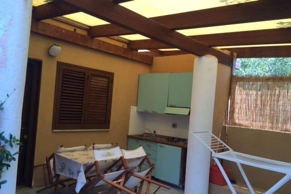 A small kitchen with a table and chairs, a window with blinds, and a wooden ceiling structure.