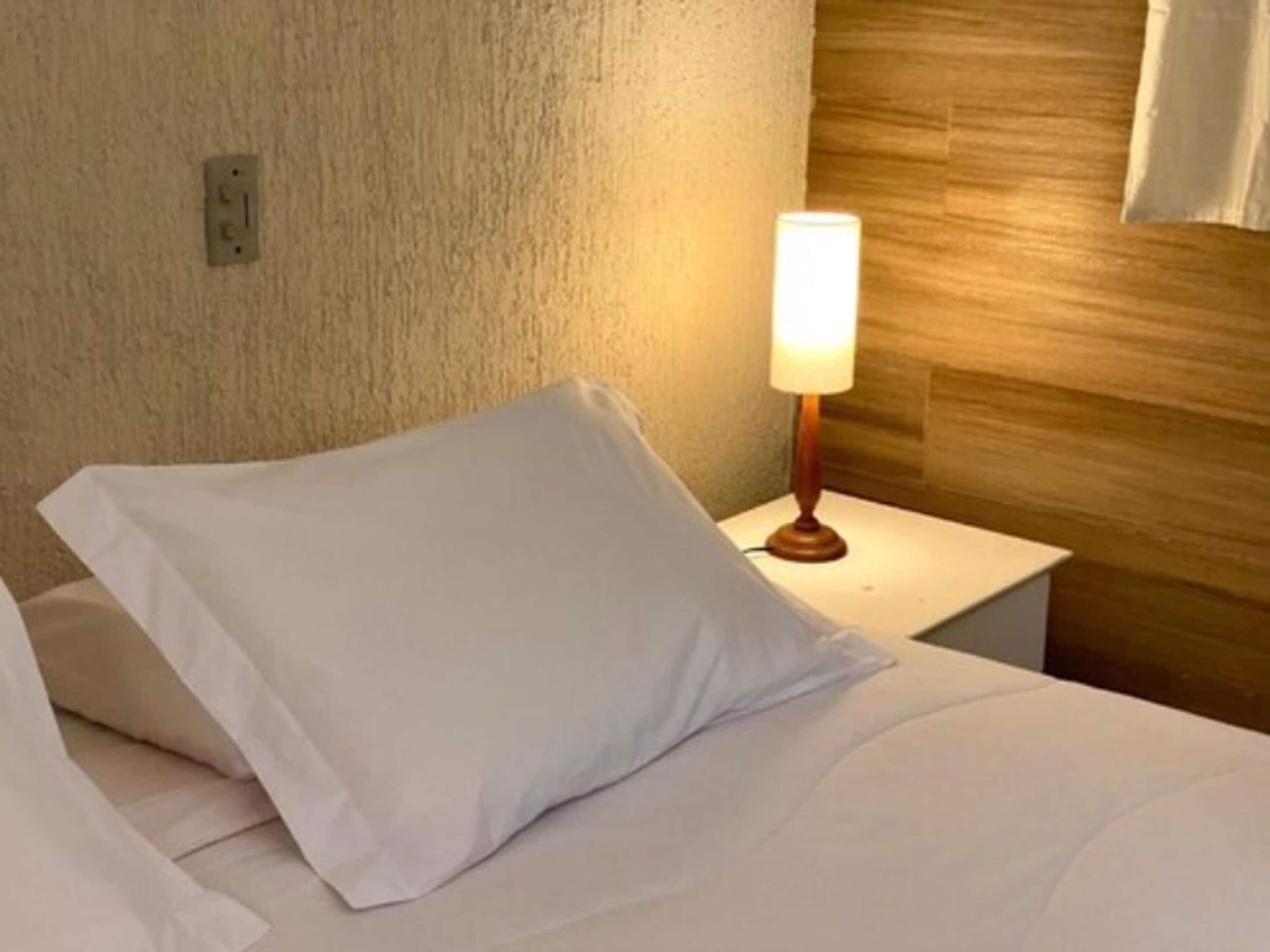 Une chambre d’hôtel avec un lit, une table de chevet, une lampe et un mur à texture.