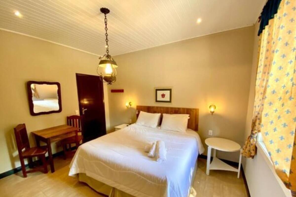 Una habitación de hotel con una cama grande, un escritorio de madera, una silla, una mesita redonda y un espejo en la pared.