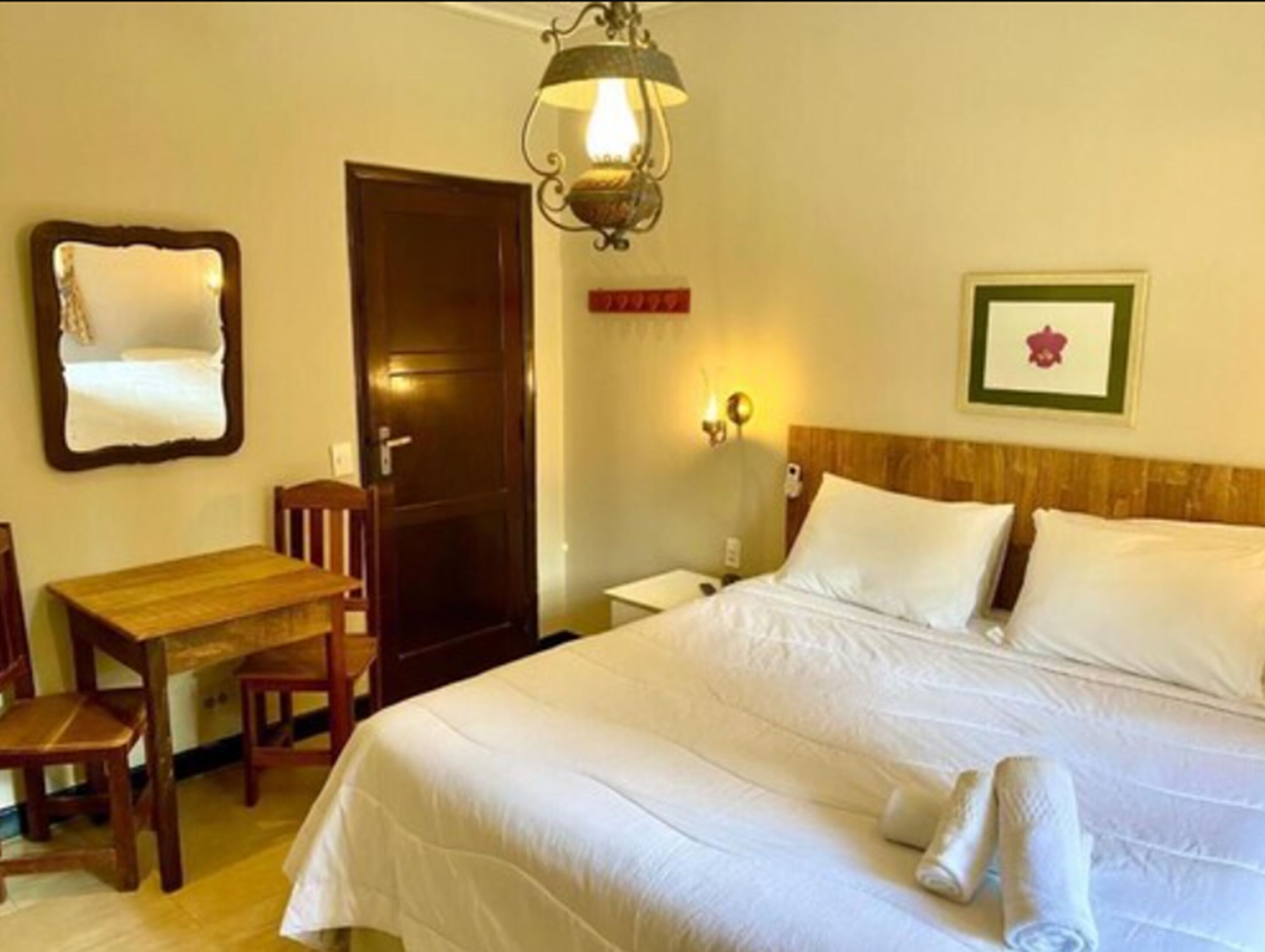 A hotel room with a bed, a desk, a chair, a door, and a wall-mounted light fixture.
