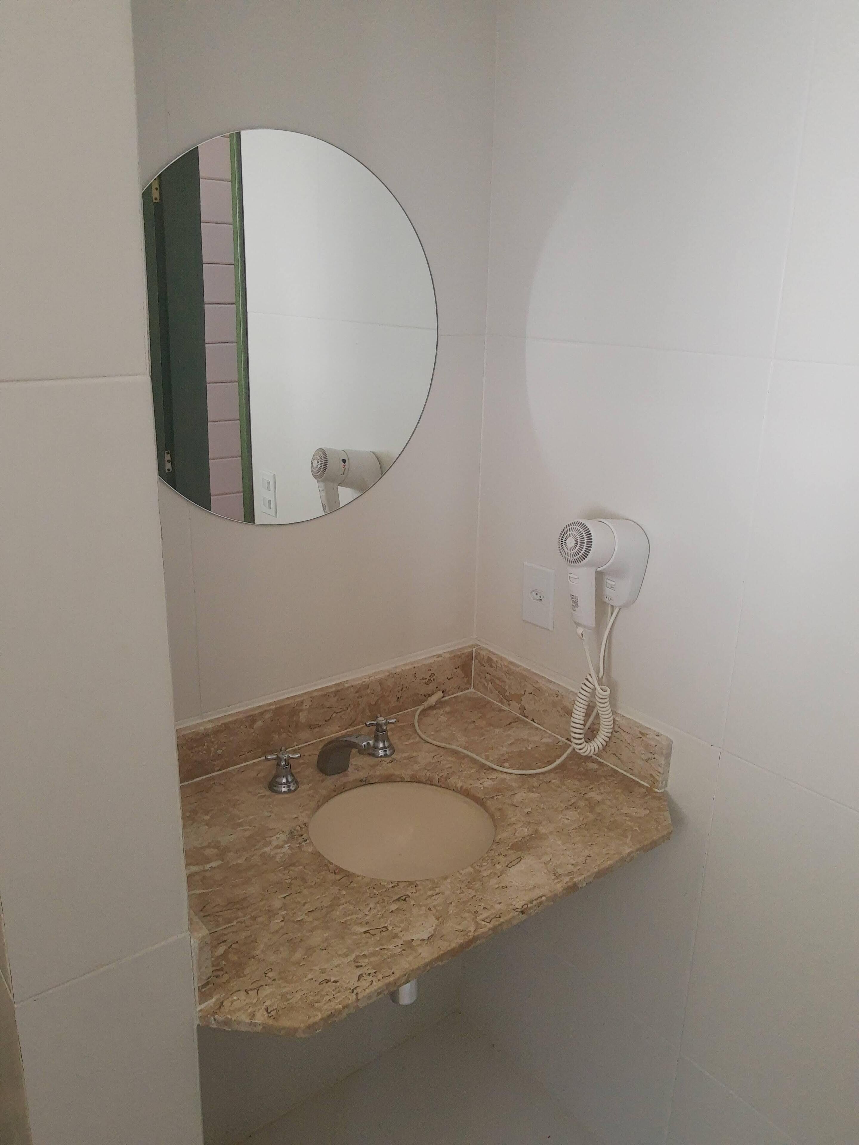 Um banheiro com pia de mármore, espelho redondo, secador de cabelo e porta-toalhas.