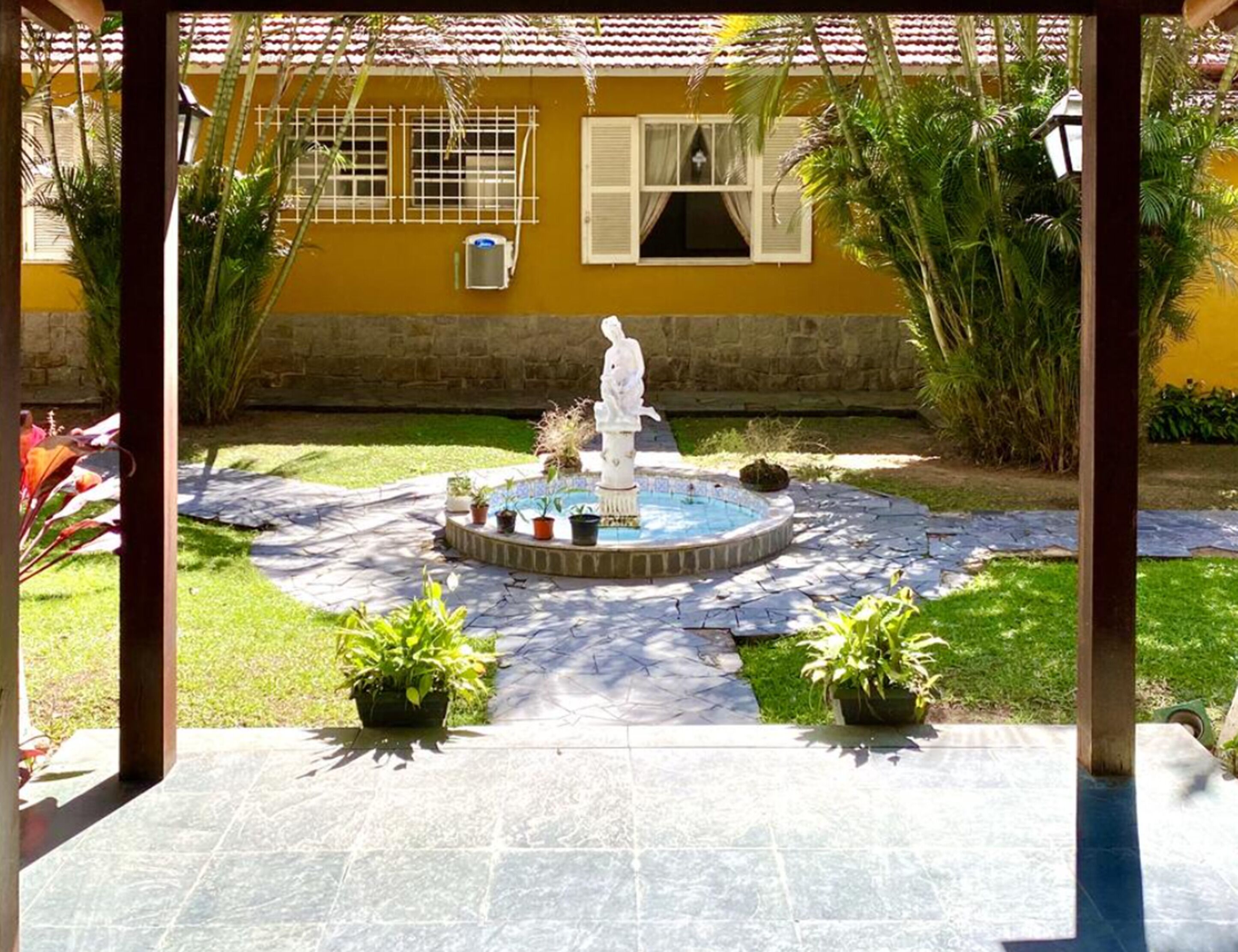 Un patio con una fuente, plantas en macetas y un edificio amarillo al fondo.
