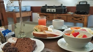 A breakfast setting with a variety of food items, including a slice of cake, a sandwich, a bowl of fruit, and a glass of juice.