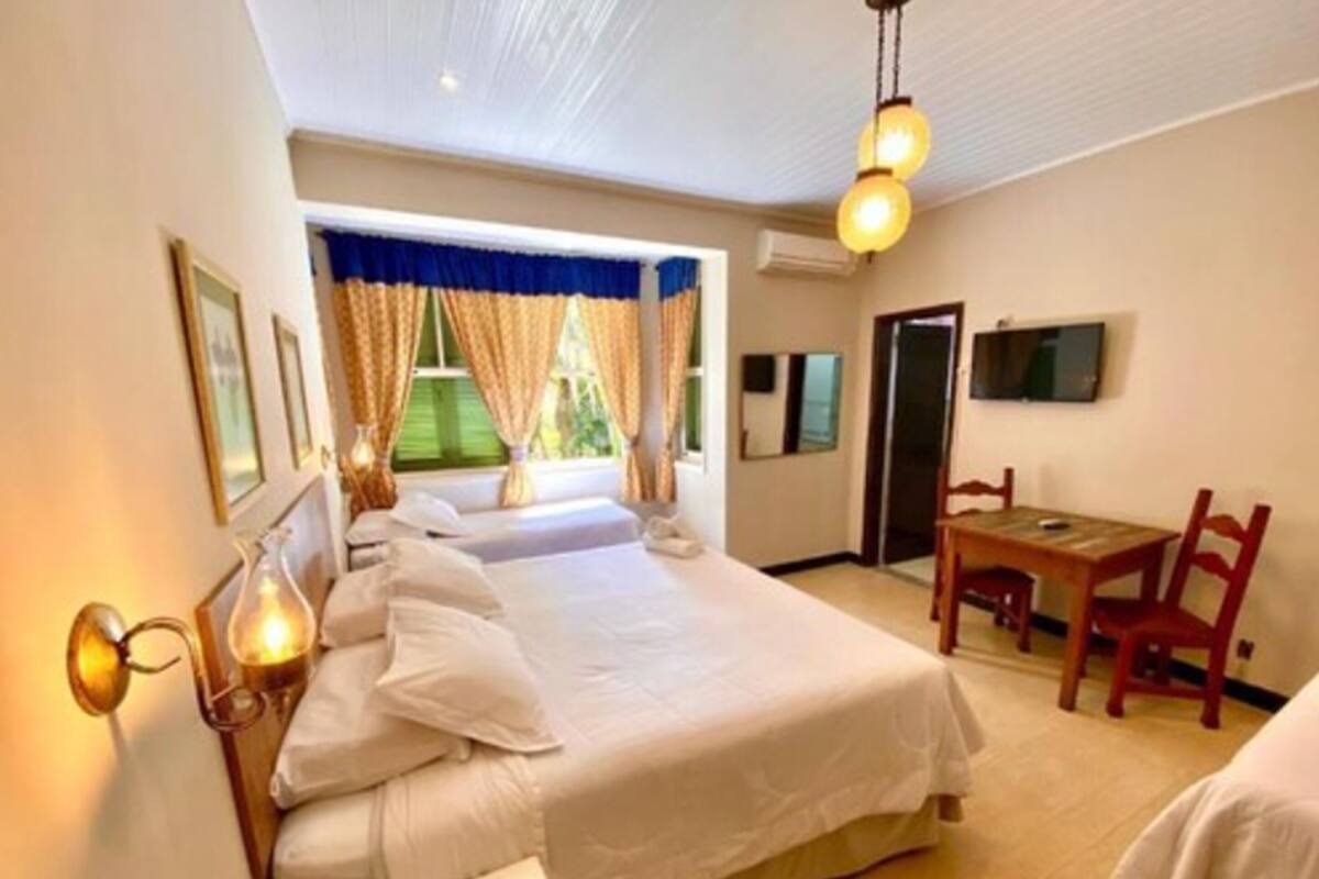 Una habitación de hotel con una cama grande, un escritorio con silla, televisión y ventana con cortinas.