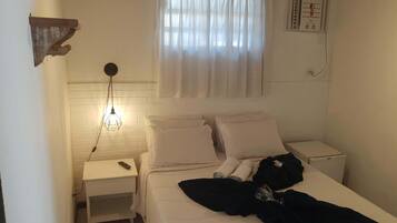 Un dormitorio con cama, mesitas de noche, un reloj de pared, una ventana con cortinas y un termostato.