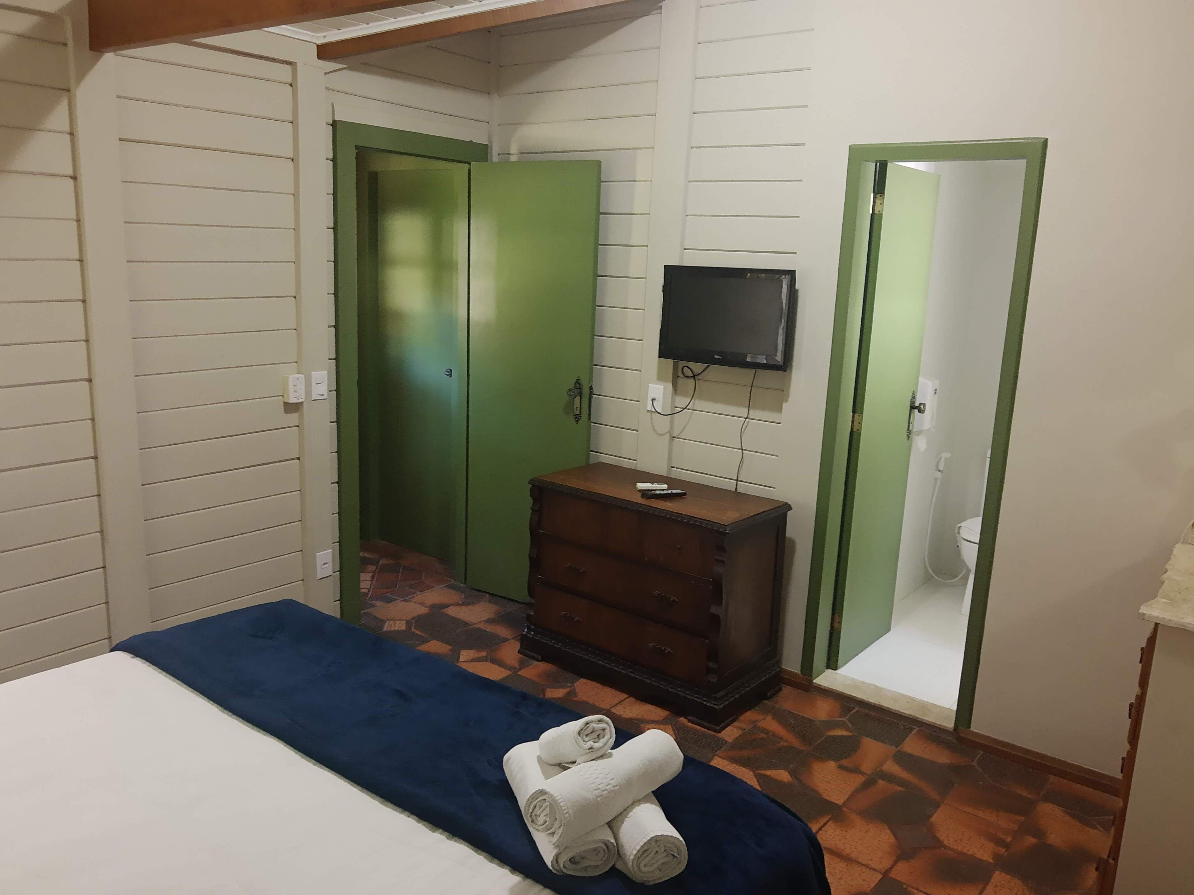 A bedroom with a bed, a dresser, a television, and green doors.