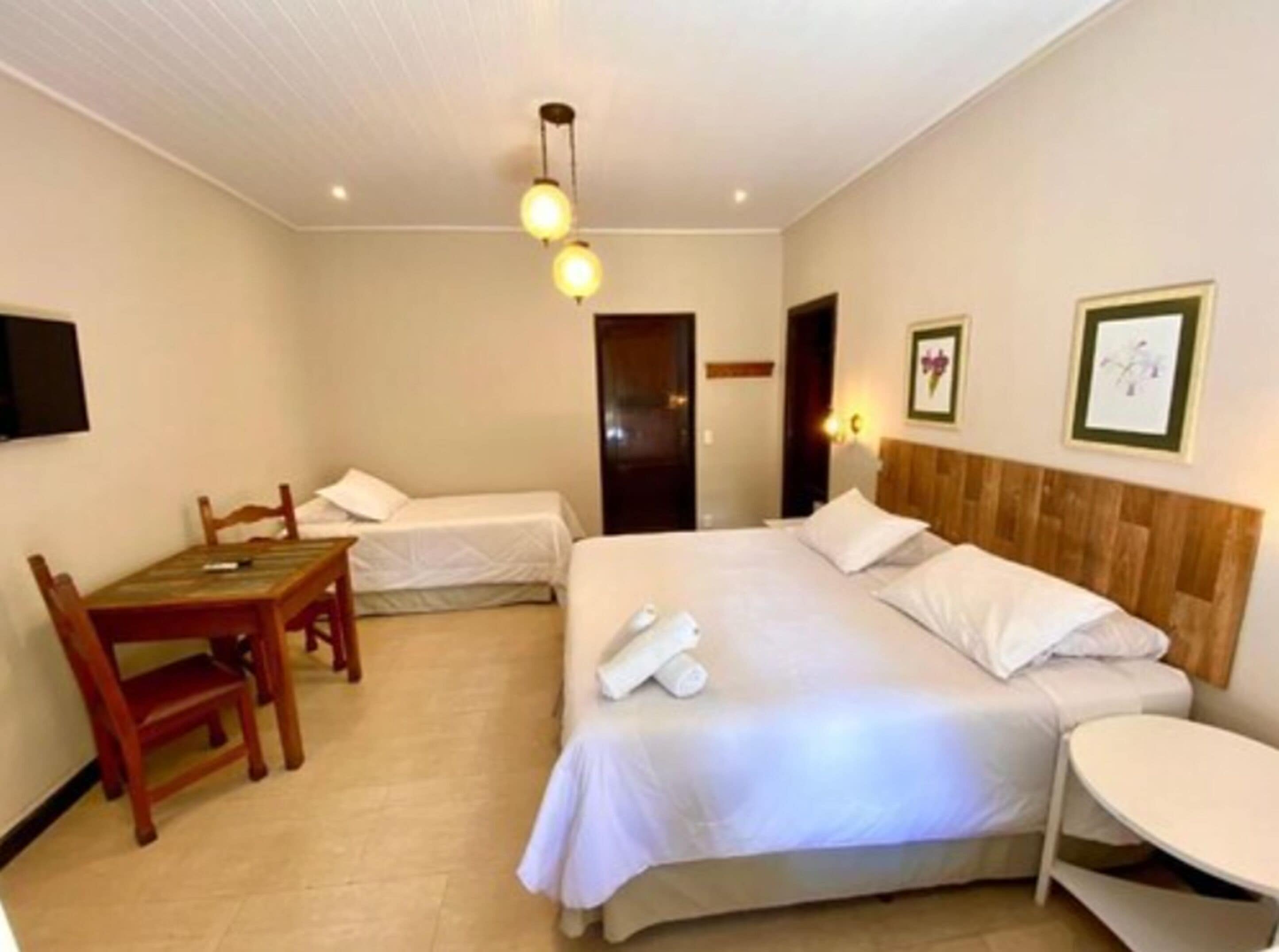 A hotel room with a large bed, a smaller bed, a desk with a chair, and a round table.