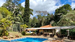 A pool area with lounge chairs, a covered patio, and a building with a tiled roof. - Hotel Vila Bavaria (Petrópolis)