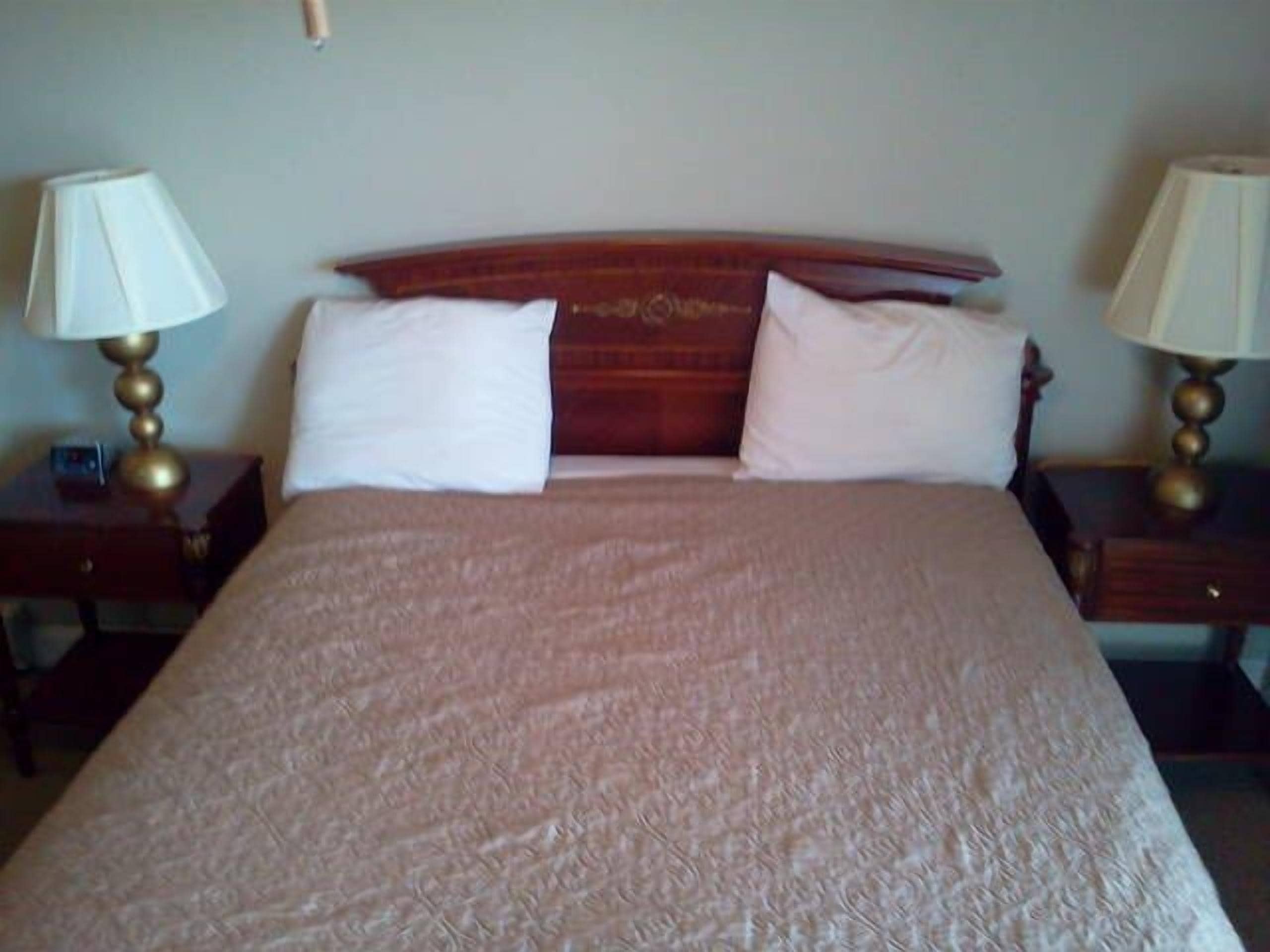 A neatly made bed with a patterned bedspread, two bedside tables with lamps, and a wooden headboard.