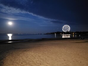 A beach at night with a large illuminated spherical structure in the distance.