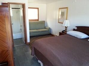 A hotel room with a bed, a sofa, a bathroom with a shower, and a window.