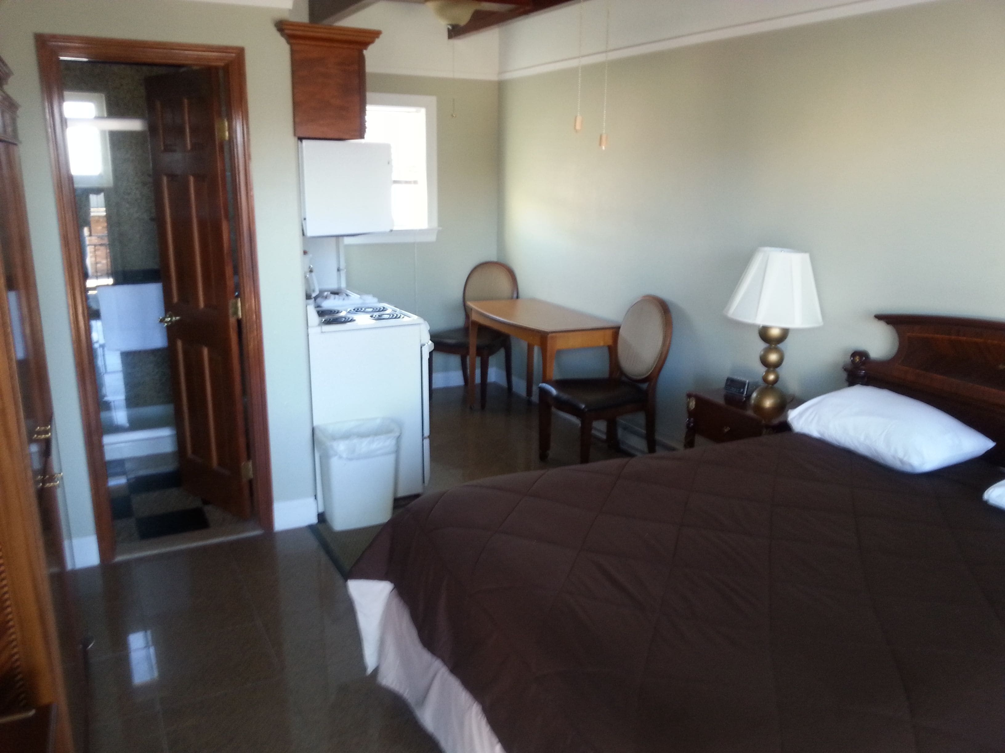 Una habitación de hotel con cama, escritorio, silla, una mesita y una lámpara.