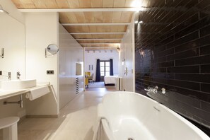 A modern bathroom with a white bathtub, a large mirror, and a sink. There is a wooden ceiling and a black tiled wall.
