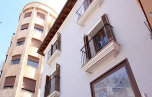A multi-story building with balconies and a large window with the text "mas Bosch".