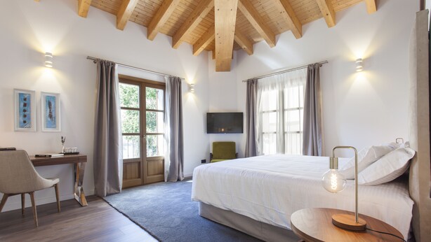 A bedroom with a bed, a desk, a chair, a TV, and a lamp.