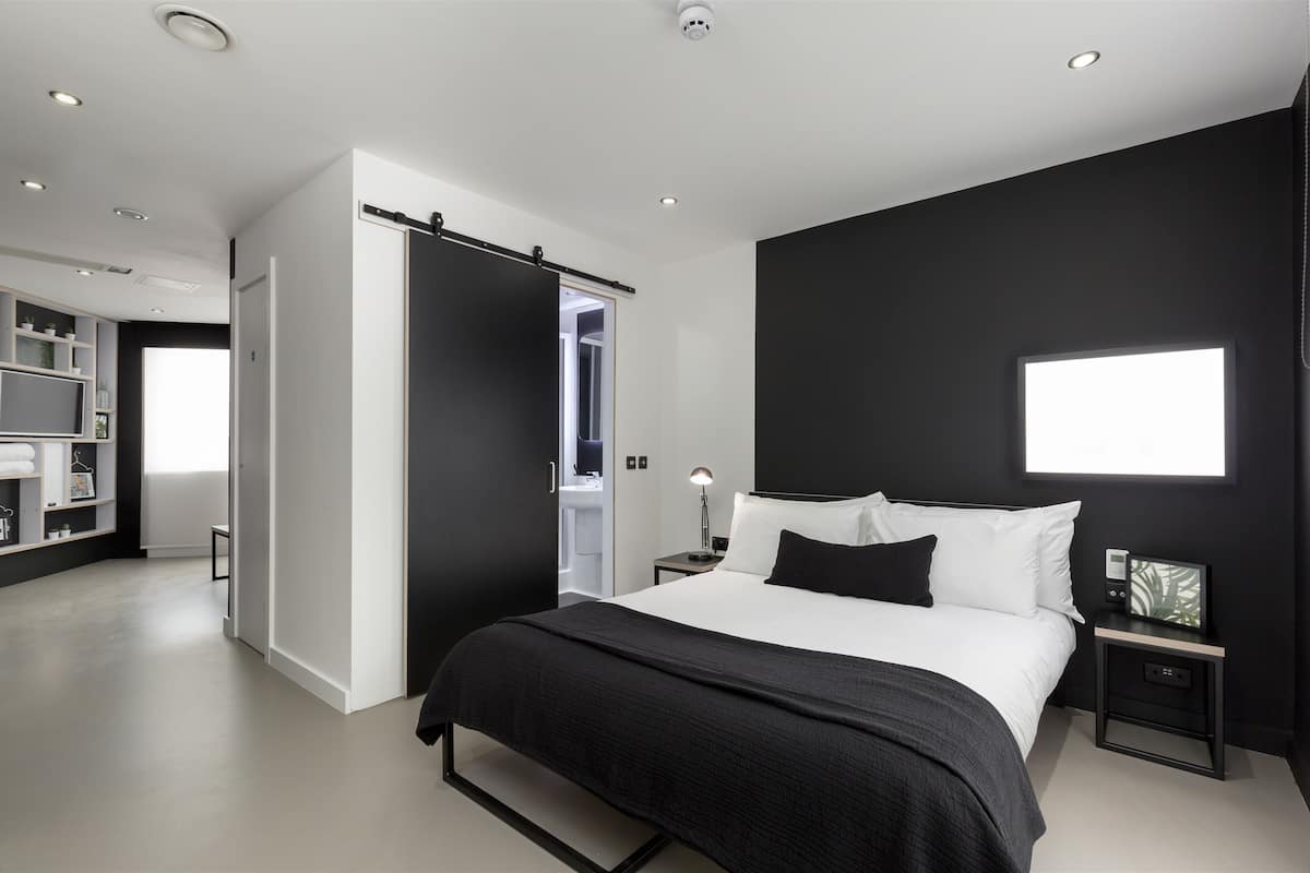 A modern bedroom with a large bed, a wardrobe, a bedside table with a lamp, and a window.