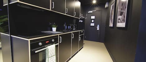 A modern kitchen with black cabinetry, a built-in oven, and a coffee machine.