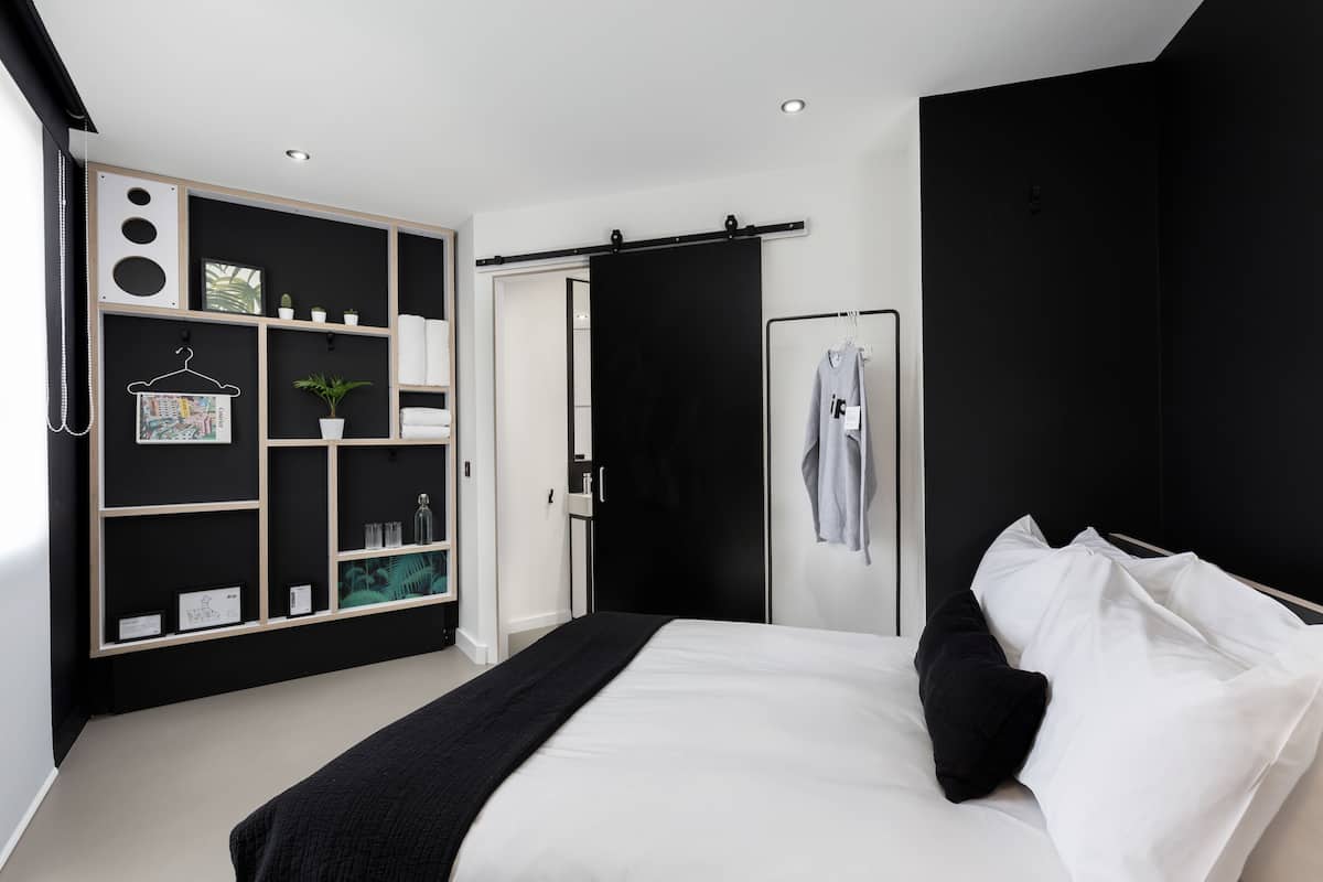 A modern bedroom with a bed, a black wardrobe, a white bedside table, and a black hanging rack.